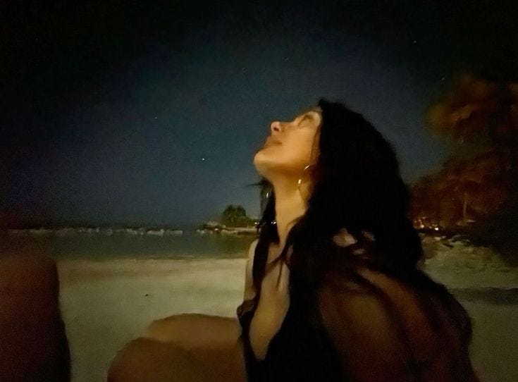 This may contain: a woman sitting on top of a beach next to the ocean at night with her eyes closed