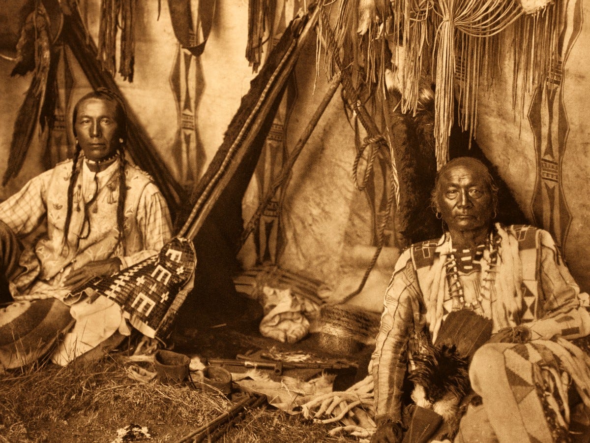 Two Native American men (Pigean band) pose inside an earth lodge, surrounded by their belongings. Edward Curtis photo, altered, 1911. Two Native American men (Pigean band) pose inside an earth lodge, surrounded by their belongings. Edward Curtis photo, altered, 1911.