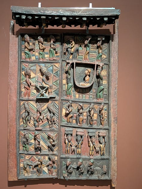 pictures taken at the gallery. Image 1 is of a door with carvings of people. Image 2: a wide picture of the galleries with wooden sculptures. Image 3: An image of a Nigerian sculptor at work in Buckingham Palace