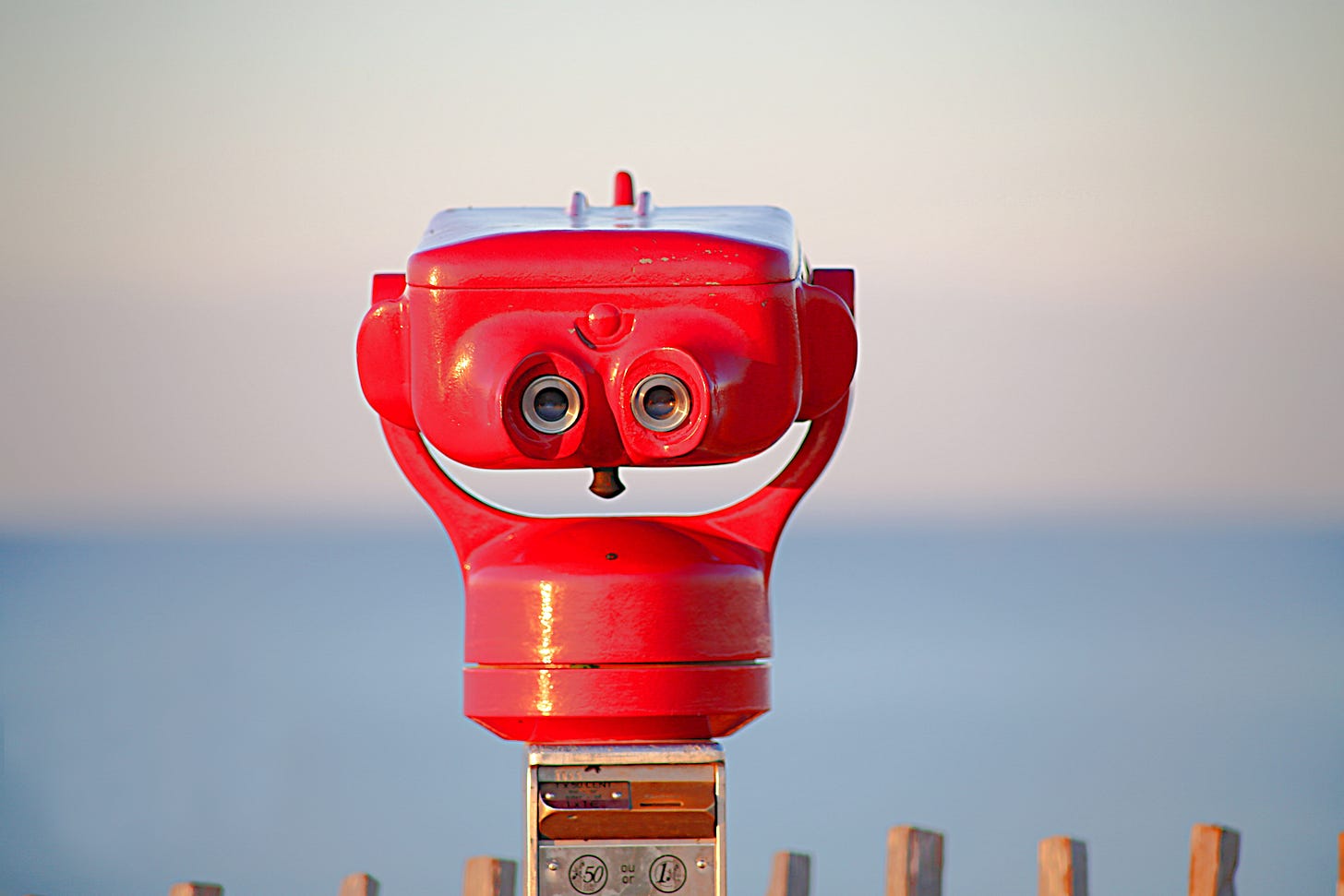 A red spotting scope pointed towards a hazy horizon over a calm blue sea
