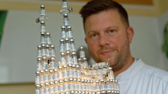 Gesundheit: Der Kölner Arzt Bastian Kirsch sitzt neben seinem Modell des Kölner Doms aus leeren Impfflaschen.