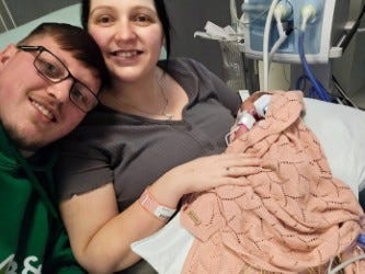 A Man and a woman with a tiny newborn baby in hospital with tubes and machines all around.