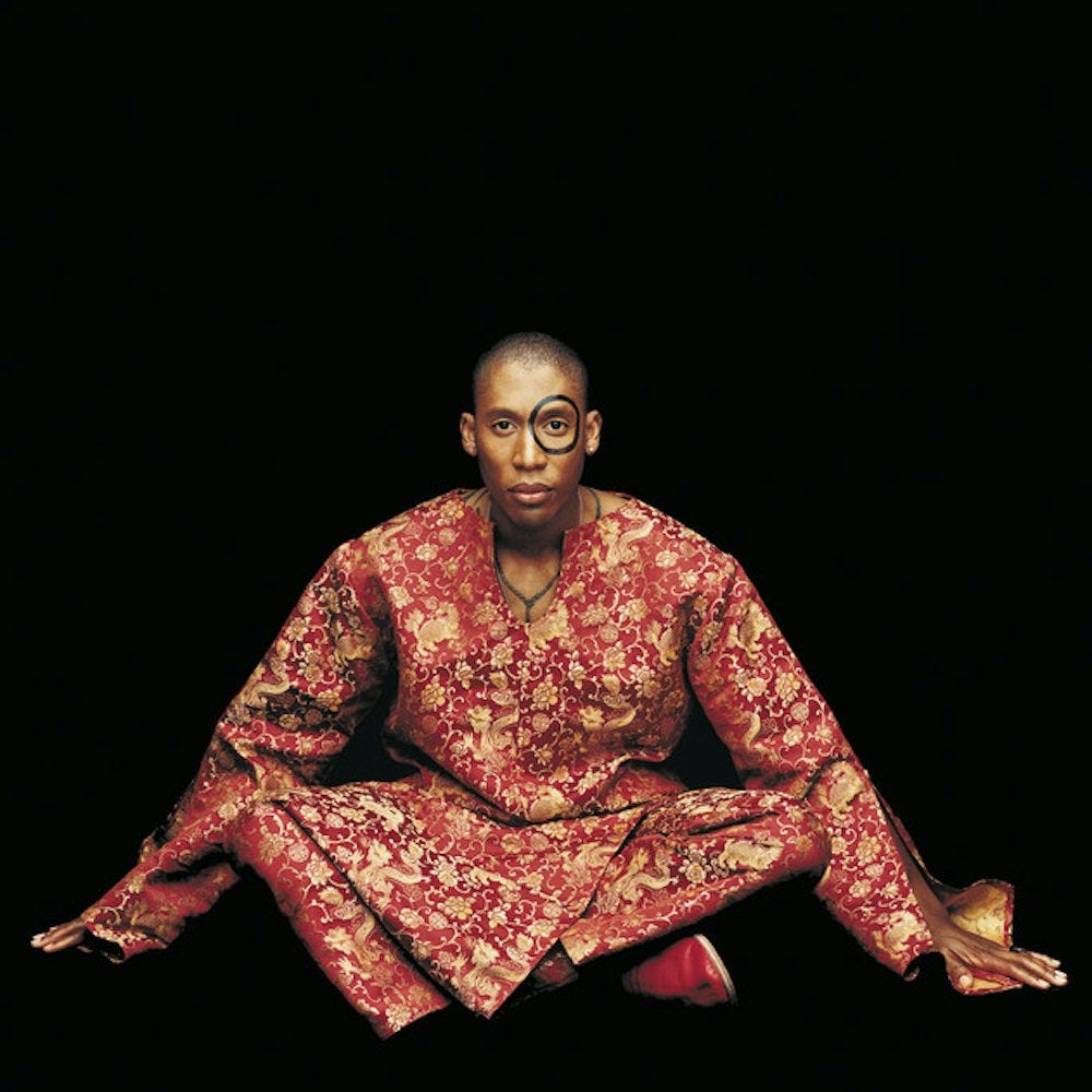 Cover art of the album "Instant Vintage" by Raphael Saadiq. He sits cross legged in a red and gold brocade gown in front of a black background. A black circle has been painted around his eye.