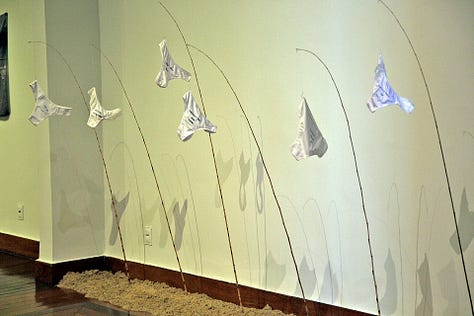 Instalação artística de Clara Salles traz calcinhas penduradas em varas de pescar, fixadas na areia no chão. Nas calcinhas, estão bordadas transcrições de juras de amor e textos que testemunham encontros amorosos explosivos.