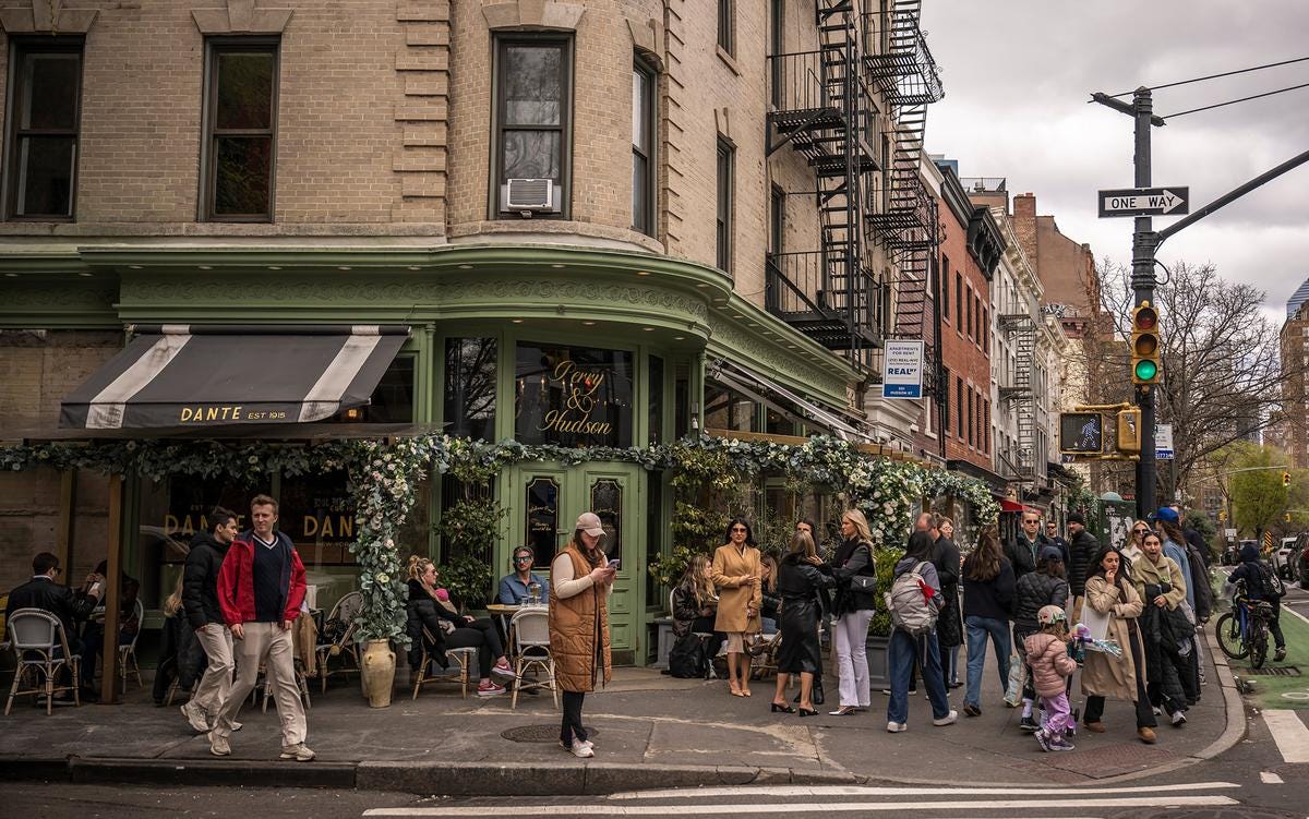 Photo of a busy street corner with people gathering outside a cafe named Dante in a city setting on a cloudy day.