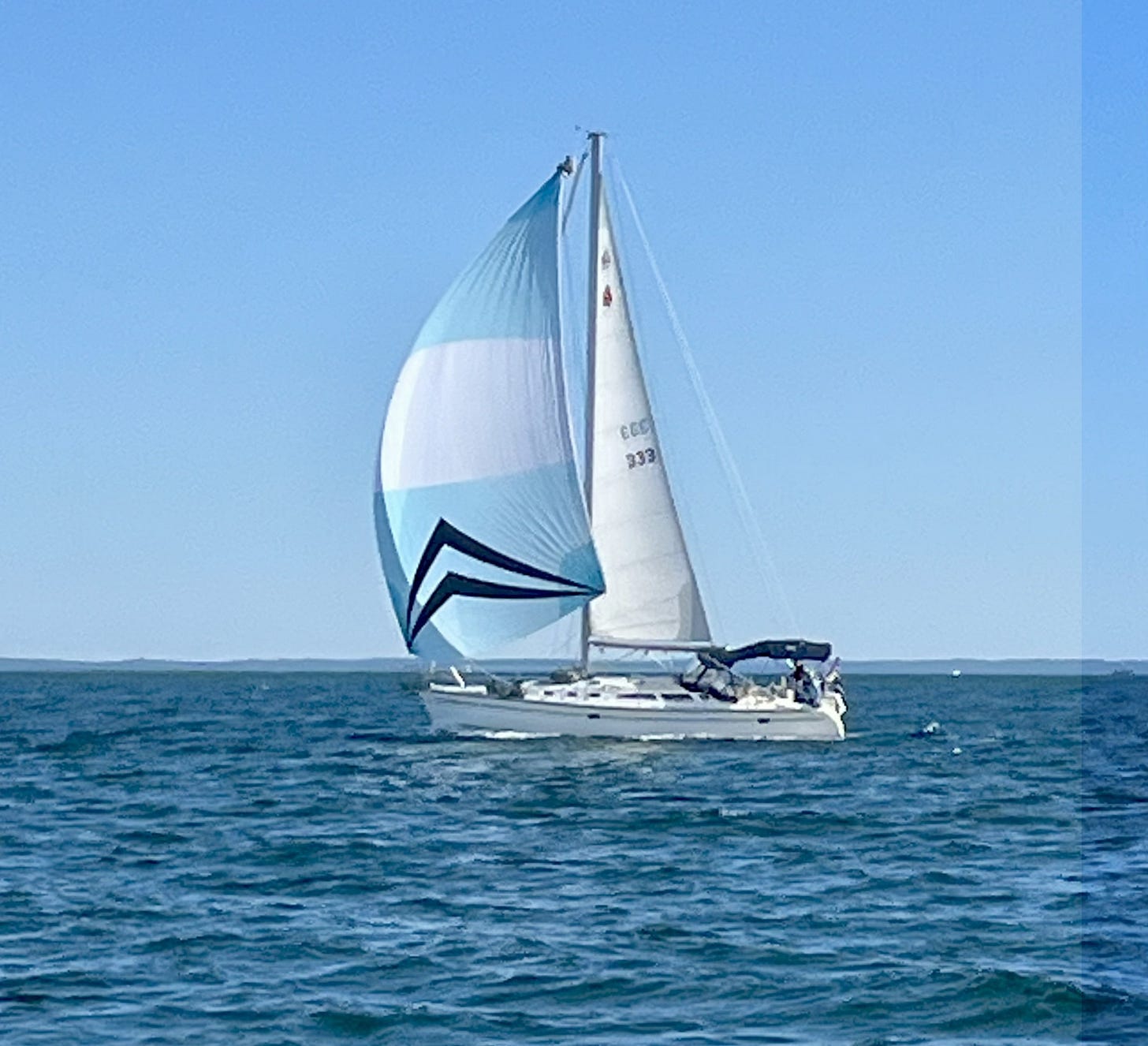 White sailboat under full sail under a blue sky and calm sea