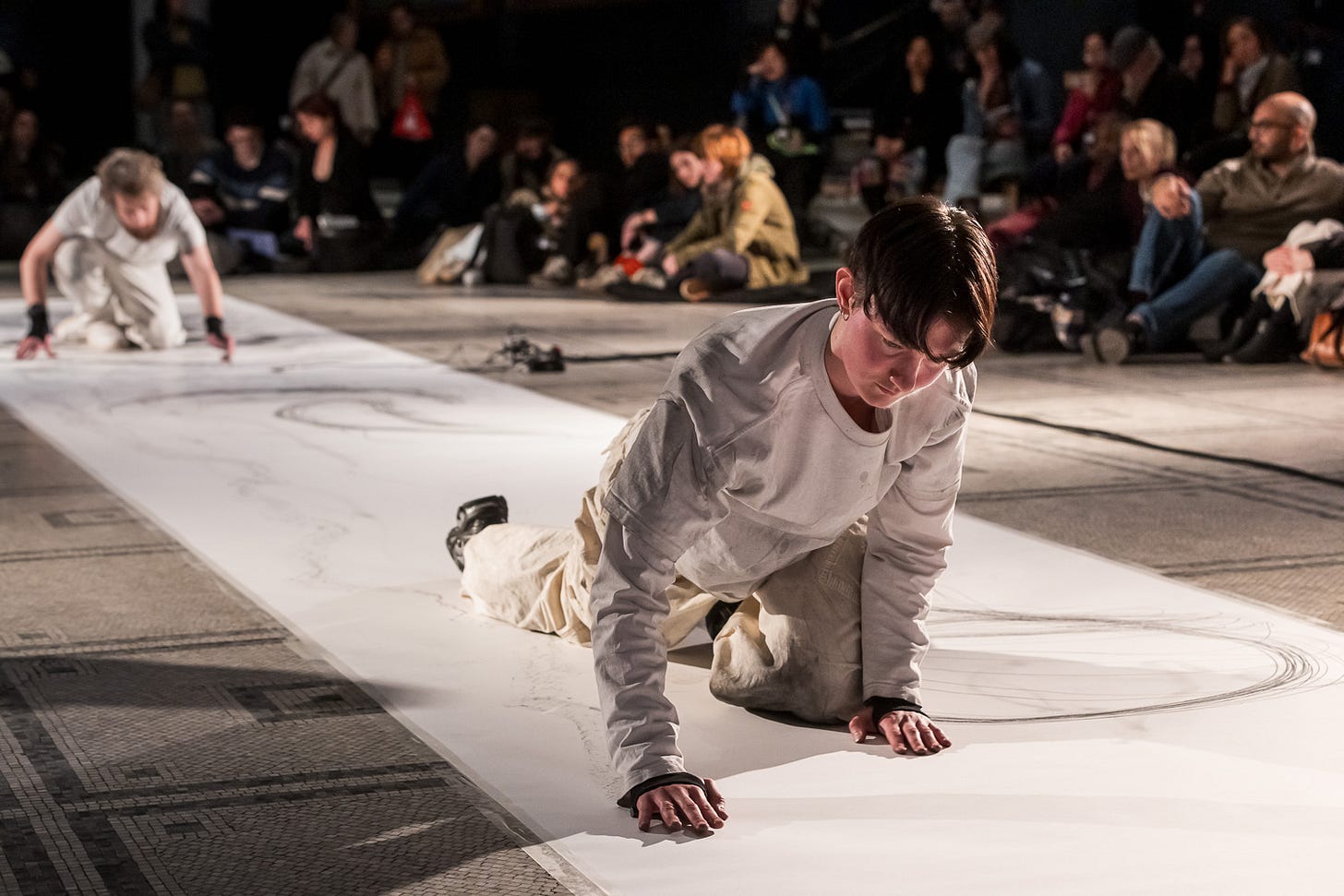 ‘Practicing in Parallel’ artists Xan Dye and Gerald Curtis mark making on paper on the ground with audience members in the background. 