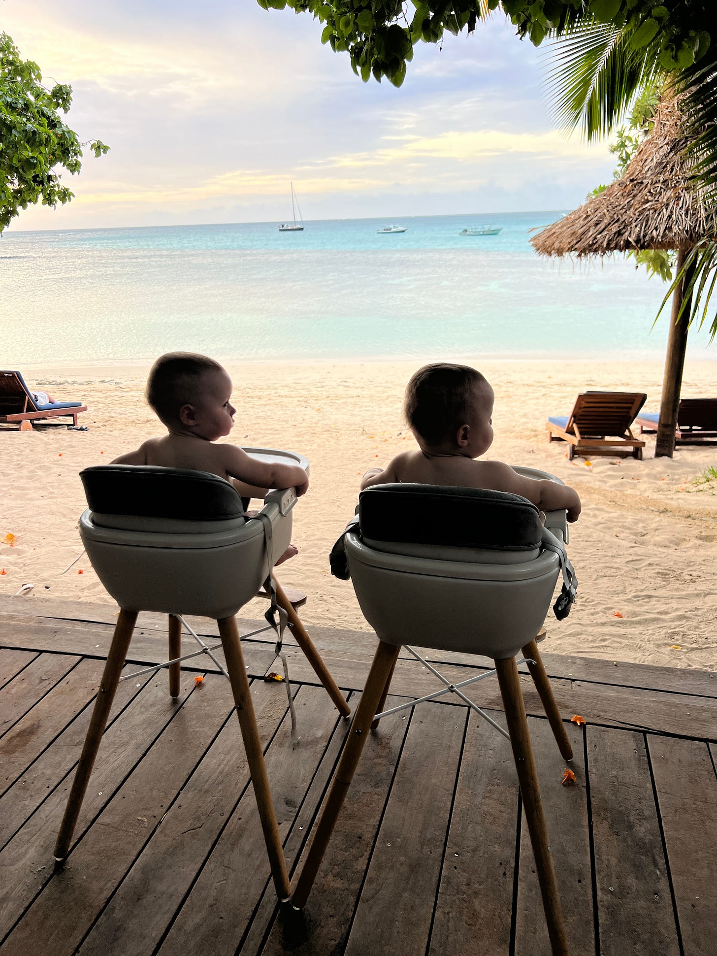 two babies sitting in high chairs facing the ocean