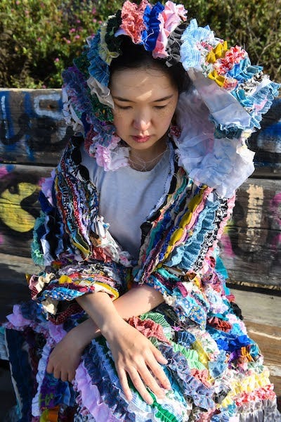 Woman wearing a hooded jacket made of gathered recycled cloths by Mira Musank