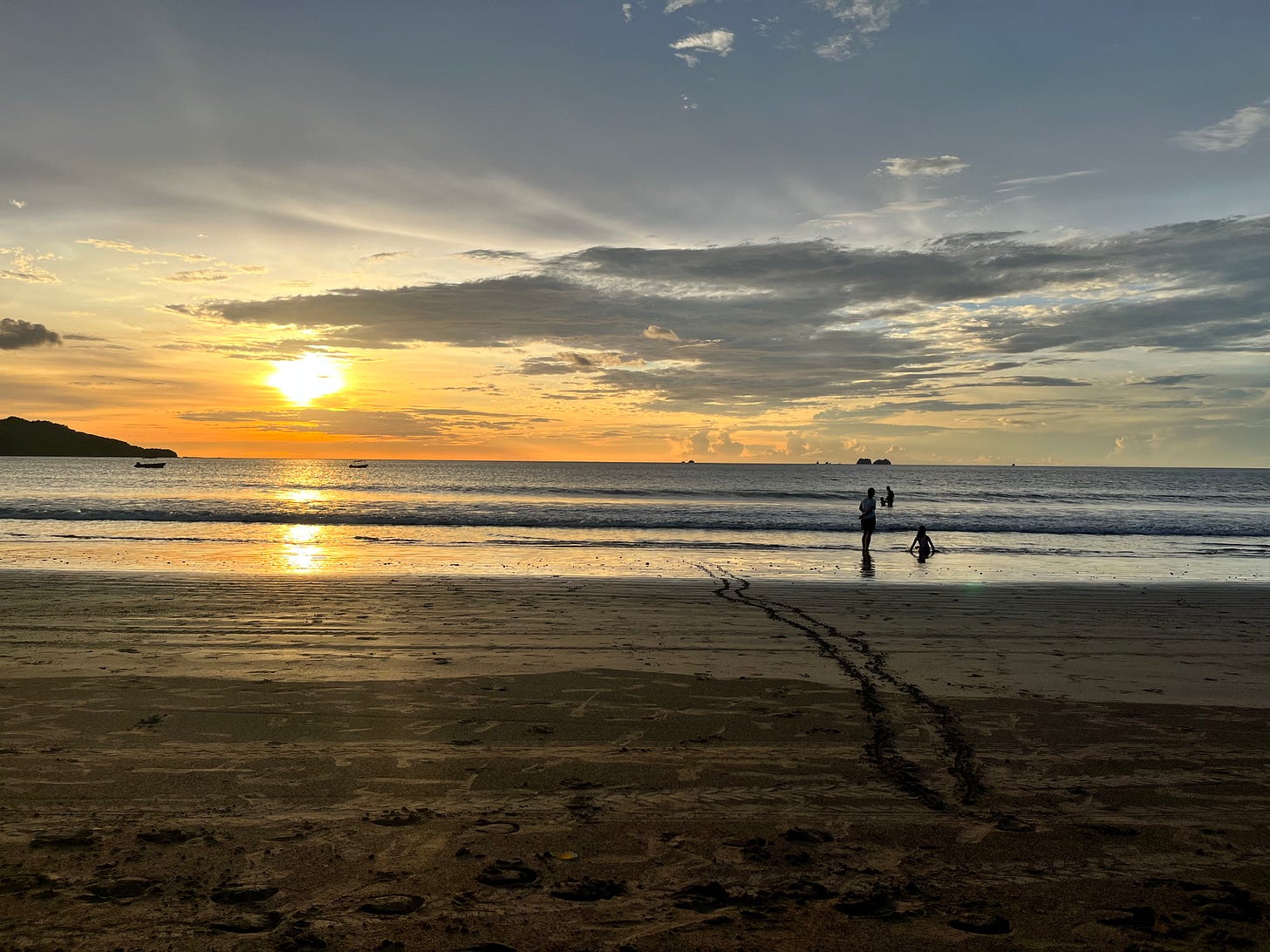 Sunset on the beach with two people by water's edge.