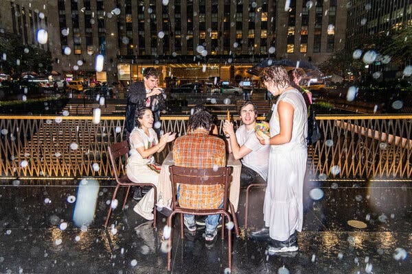 Five people at an outdoor table on a plaza overlooking a city street in the rain.