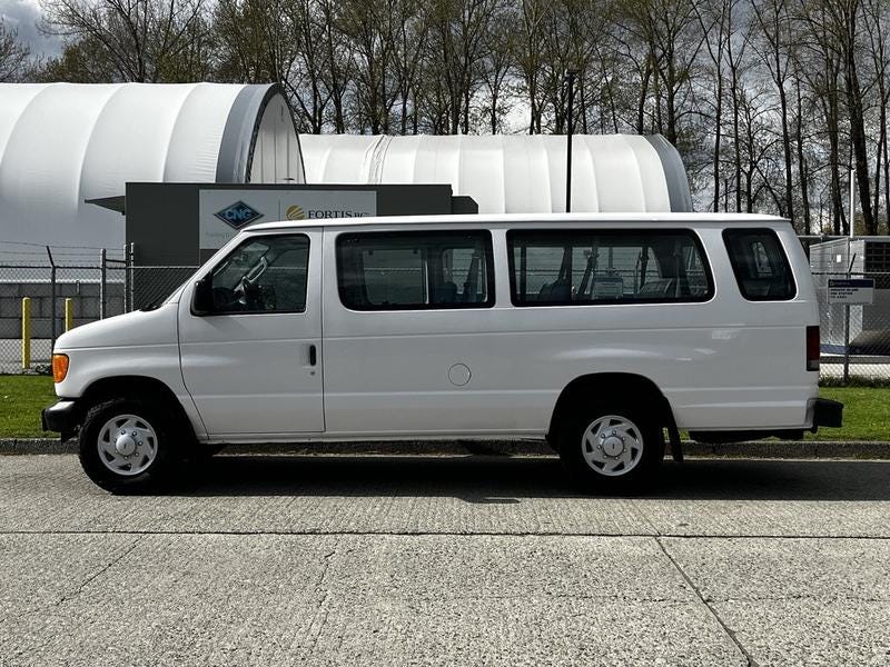 A white 2004 Ford Econoline van is parked facing the left with sliding doors and a simple design showing a clean exterior and standard wheels