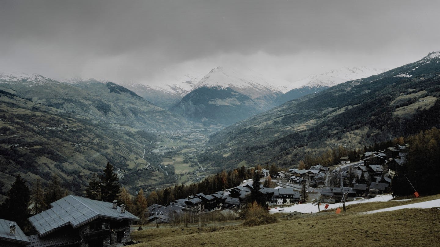 Foto di una montagna con edifici, un po' di neve, nuvole in alto e una valle sottostante Foto di una montagna con edifici, un po' di neve, nuvole in alto e una valle sottostante