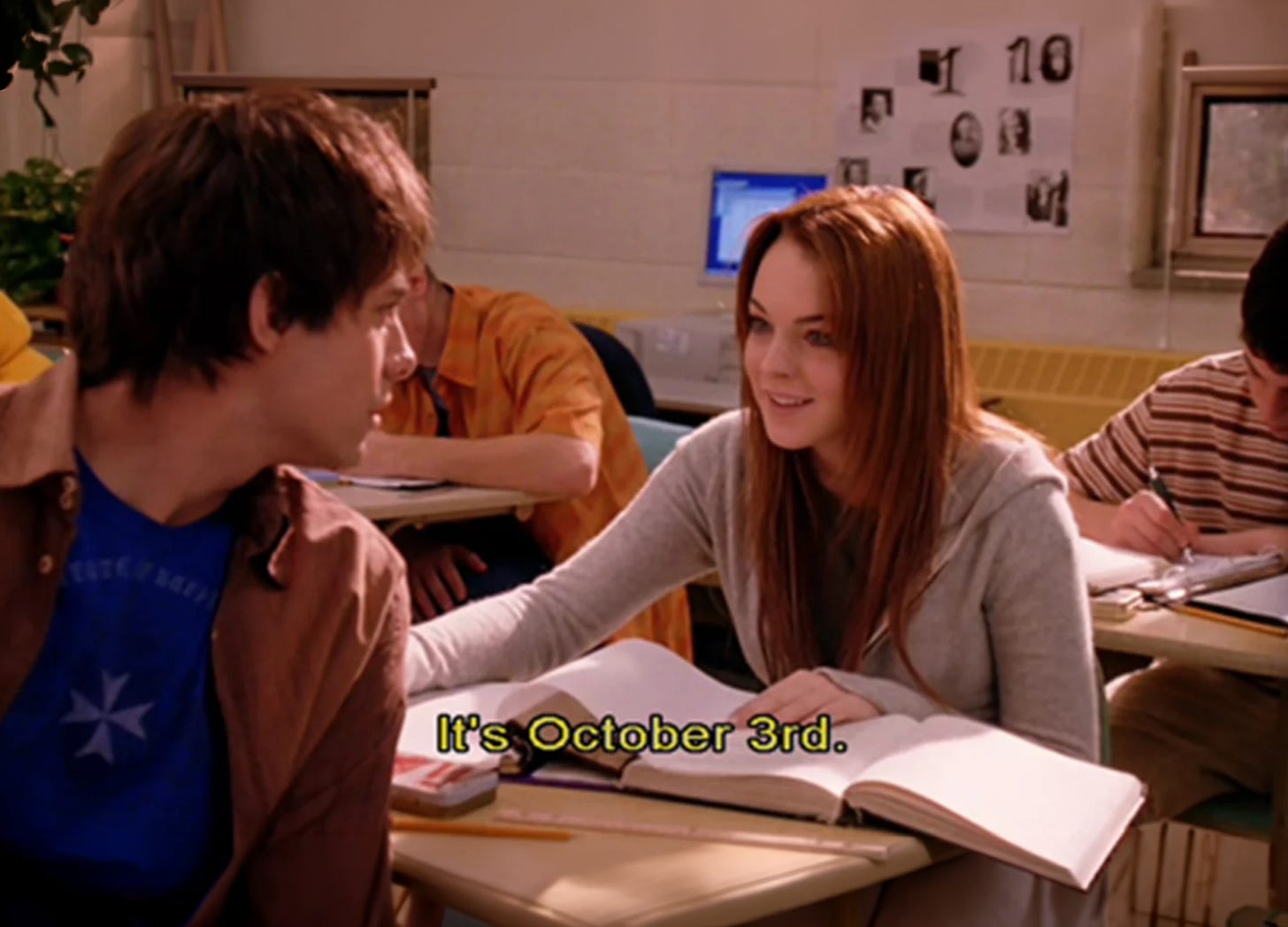 Scene from Mean Girls: a girl leans across a classroom desk toward a boy. Subtitle reads, "It's October 3rd."