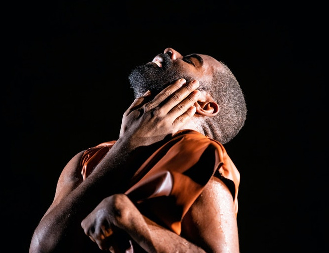 Jerron Herman gazes up with his eyes closed under dramatic stage lighting