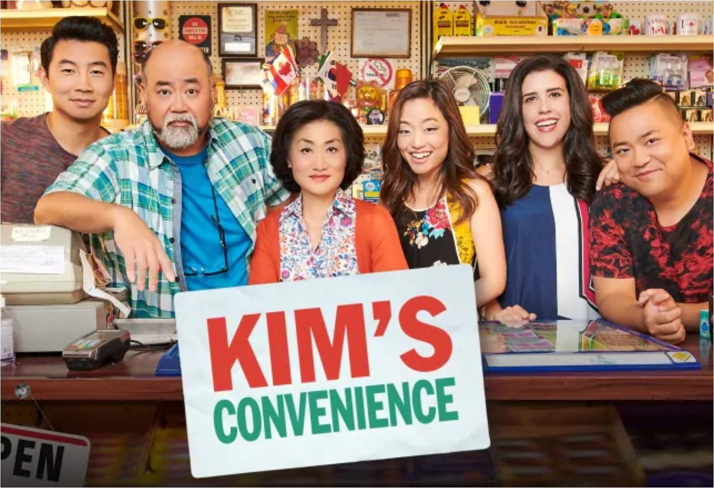 Il cast di Kim's Convenience posa al bancone del minimarket in cui lavorano alcuni dei protagonisti. I genitori “Appa” (Paul Sun-Hyung Lee) e “Umma” (Jean Yoon), la figlia Janet (Andrea Bang) e il figlio Jung (Simu Liu). Ci sono poi l'amico e collega di Jung, Kimchee (Andrew Phung), e la sua manager Shannon (Nicole Power).