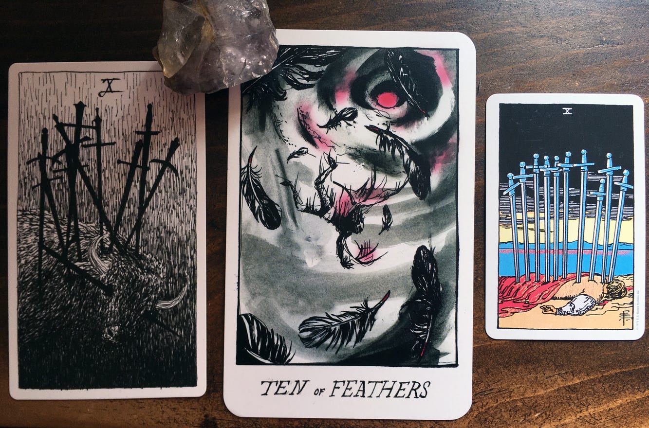 Three tarot cards on a brown wood backround. The card on the left depicts a bull stuck with ten swords. The largest card in the middle depicts a figure falling from the sky, feathers all around them. The smallest card on the right depicts a figure lying face-down on the ground with ten swords stuck in their back. Three tarot cards on a brown wood backround. The card on the left depicts a bull stuck with ten swords. The largest card in the middle depicts a figure falling from the sky, feathers all around them. The smallest card on the right depicts a figure lying face-down on the ground with ten swords stuck in their back.