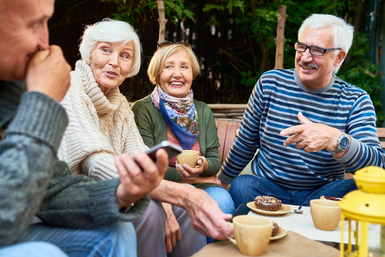 Group of cheerful seniors enjoying time together drinking tea outdoors in cafe and sharing life stories in retirement.