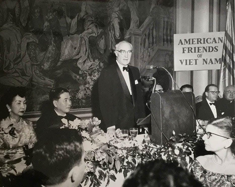 A person standing at a podium with a crowd of people

Description automatically generated