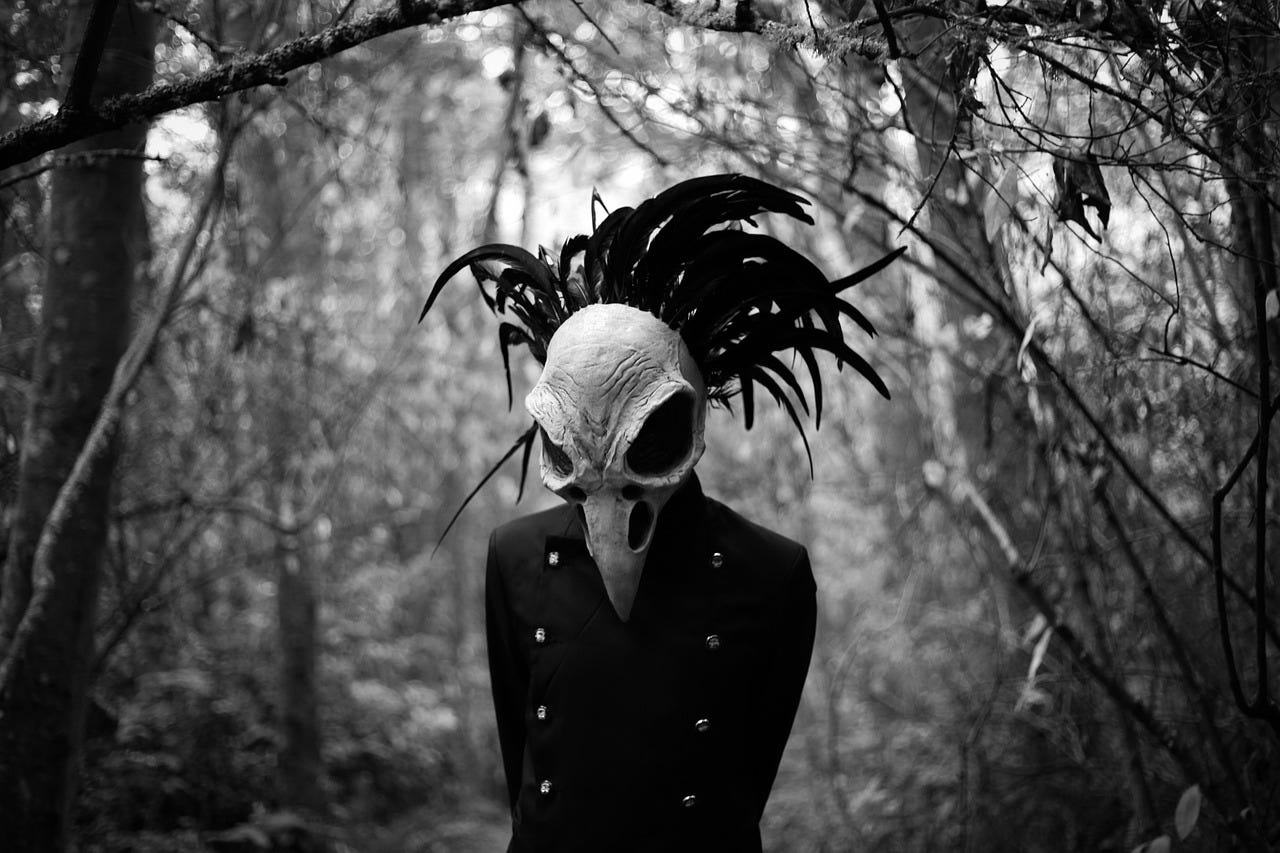 A person in the woods wears a plague mask resembling a bird skull.