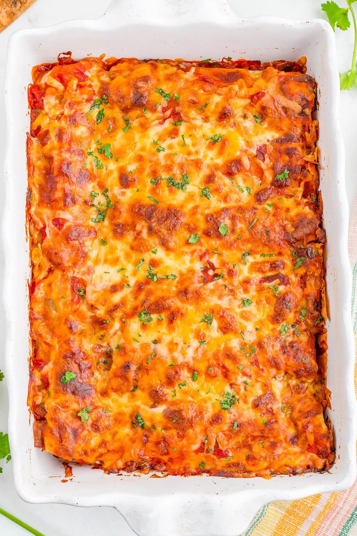 A baked casserole dish filled with golden-brown, cheesy lasagna topped with chopped herbs.