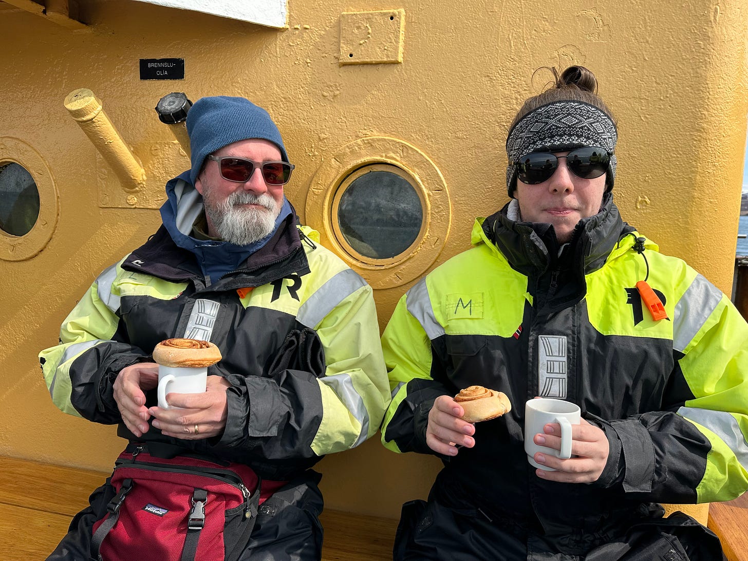 Photo of two men enjoying hot chocolate and cinnamon rolls on a wooden boat in Iceland.