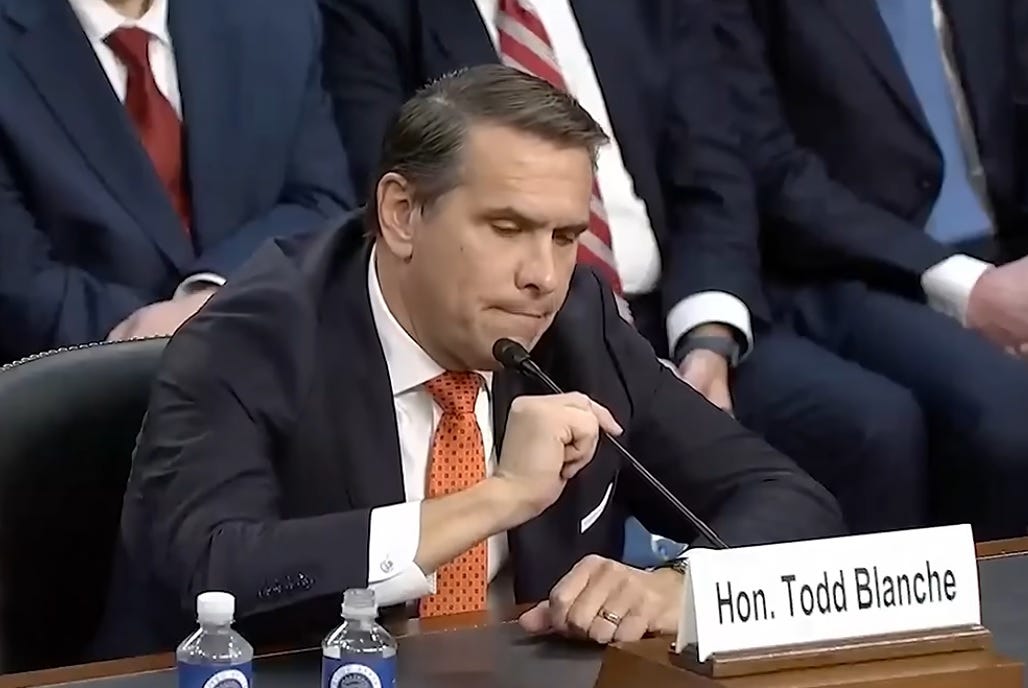 Video screenshot of Todd Blanche at his confirmation hearing, adjusting the mic on his table with a silly irritated look on his face. 