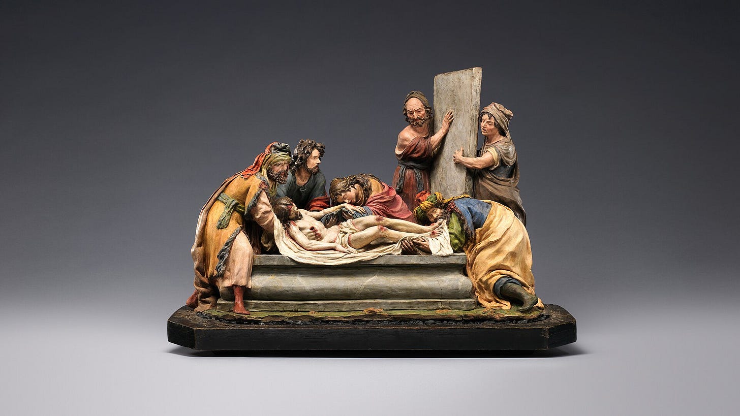 A small painted terracotta group: the body of Christ lowered into a tomb by several mourners, among them women in blue and red robes and a bearded man. A small painted terracotta group: the body of Christ lowered into a tomb by several mourners, among them women in blue and red robes and a bearded man.