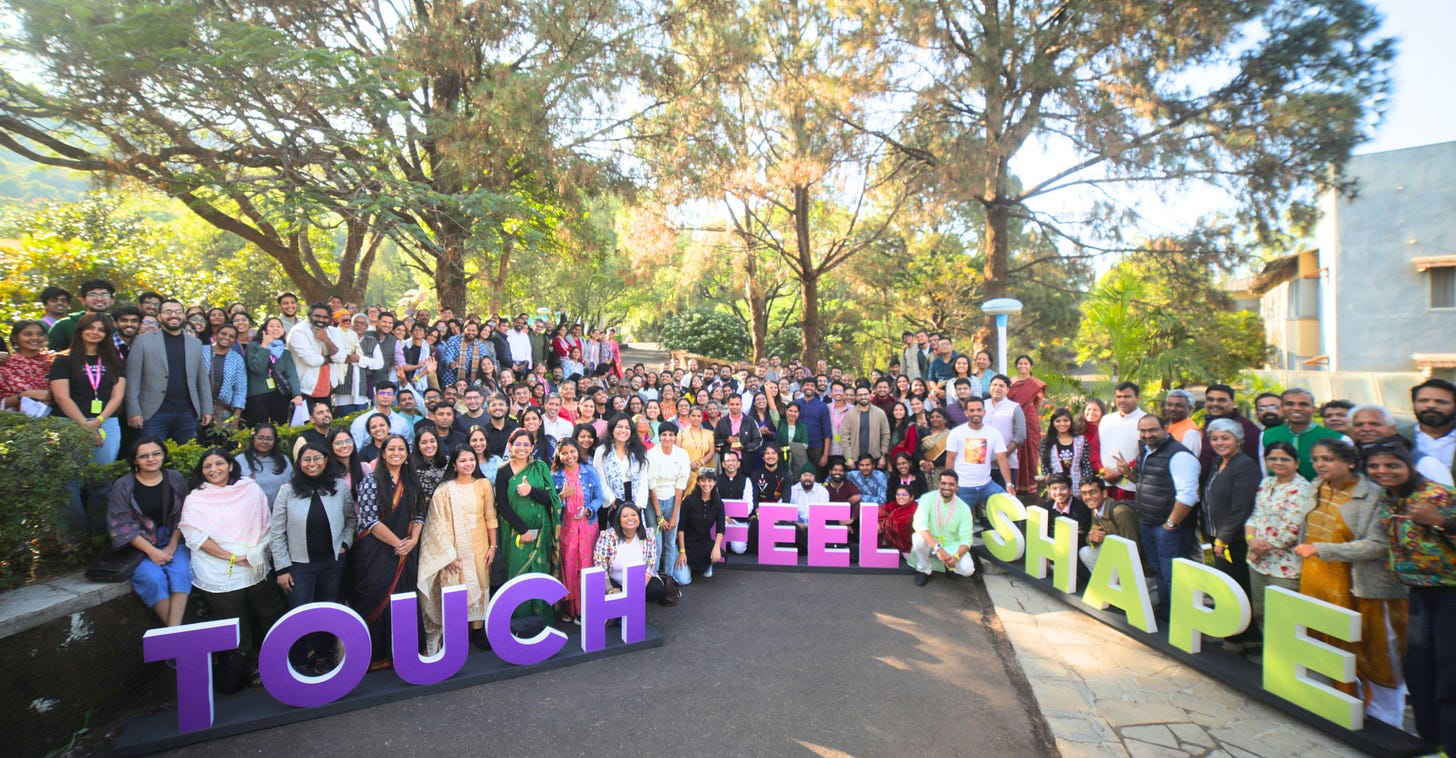 A group of over hundred people standing together in an open space with props saying the words 'Touch', 'Feel', 'Shape'