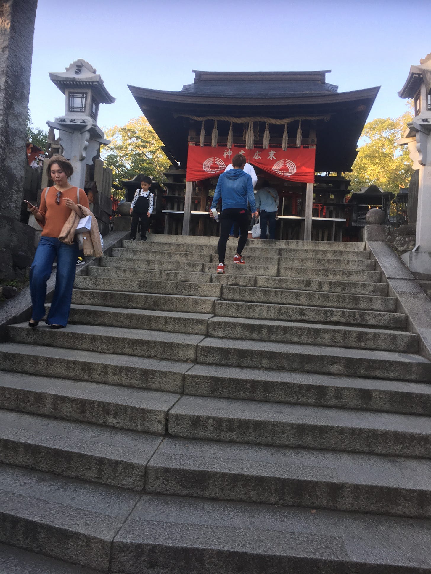 Shrine at the top of Fushimi Inari; stone steps lead up to a shrine with red curtains.  People can be seen going up and down the steps.