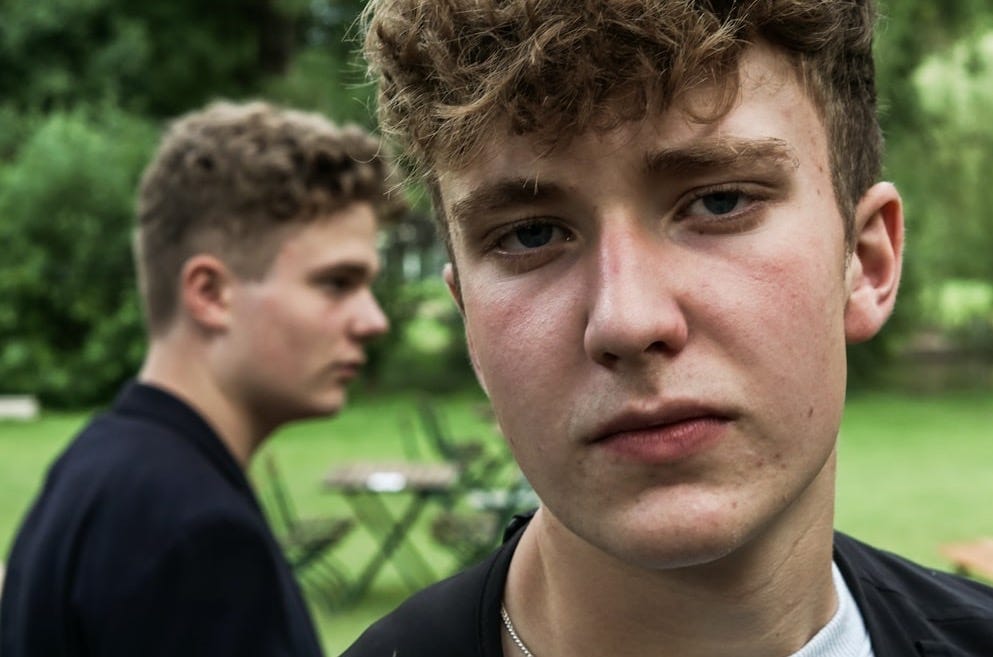 a young man standing in a park next to another man a young man standing in a park next to another man