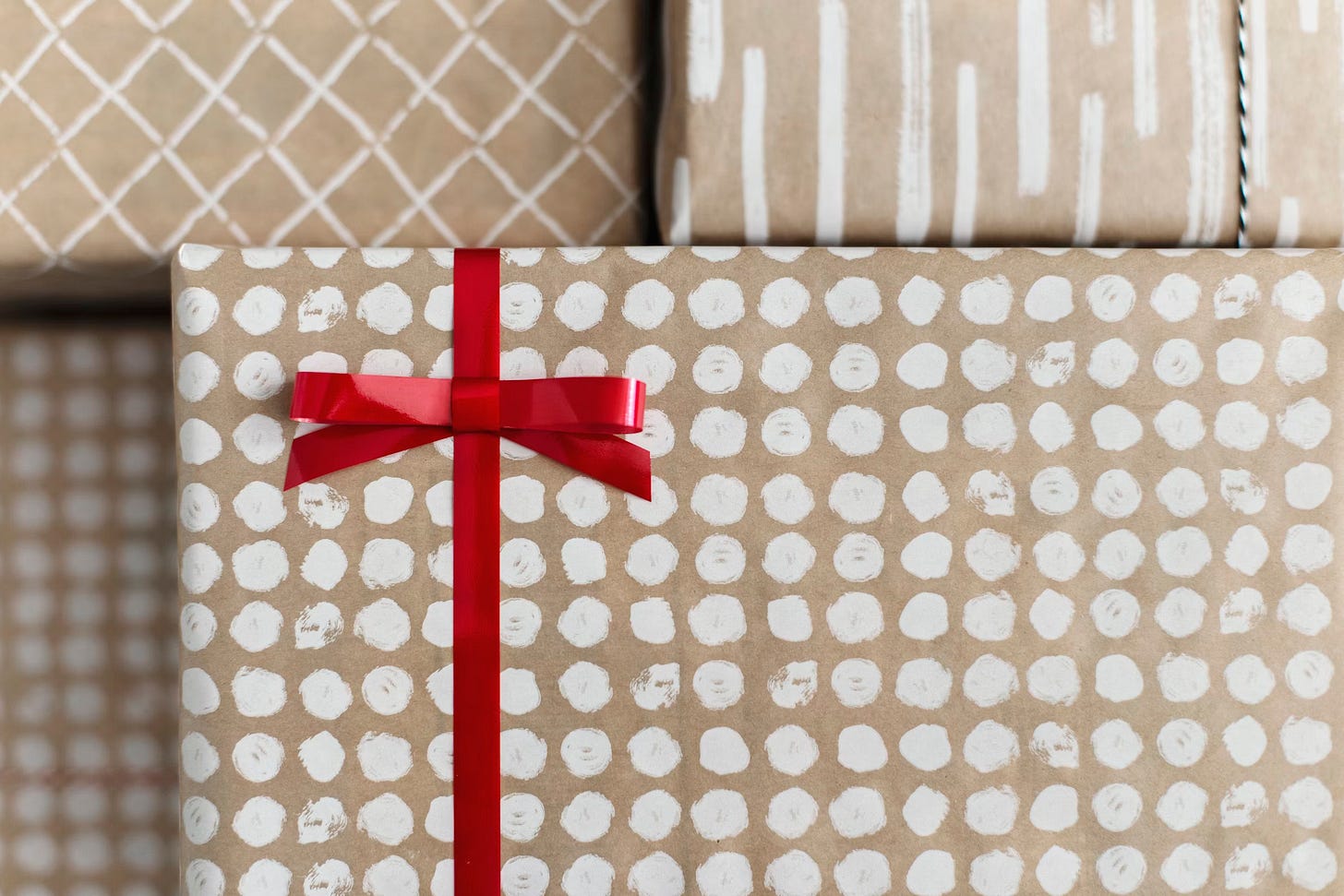 Present wrapped in brown paper with white dots, tied with a bright red ribbon. It's on top of a few other gifts wrapped in similar paper with different designs.