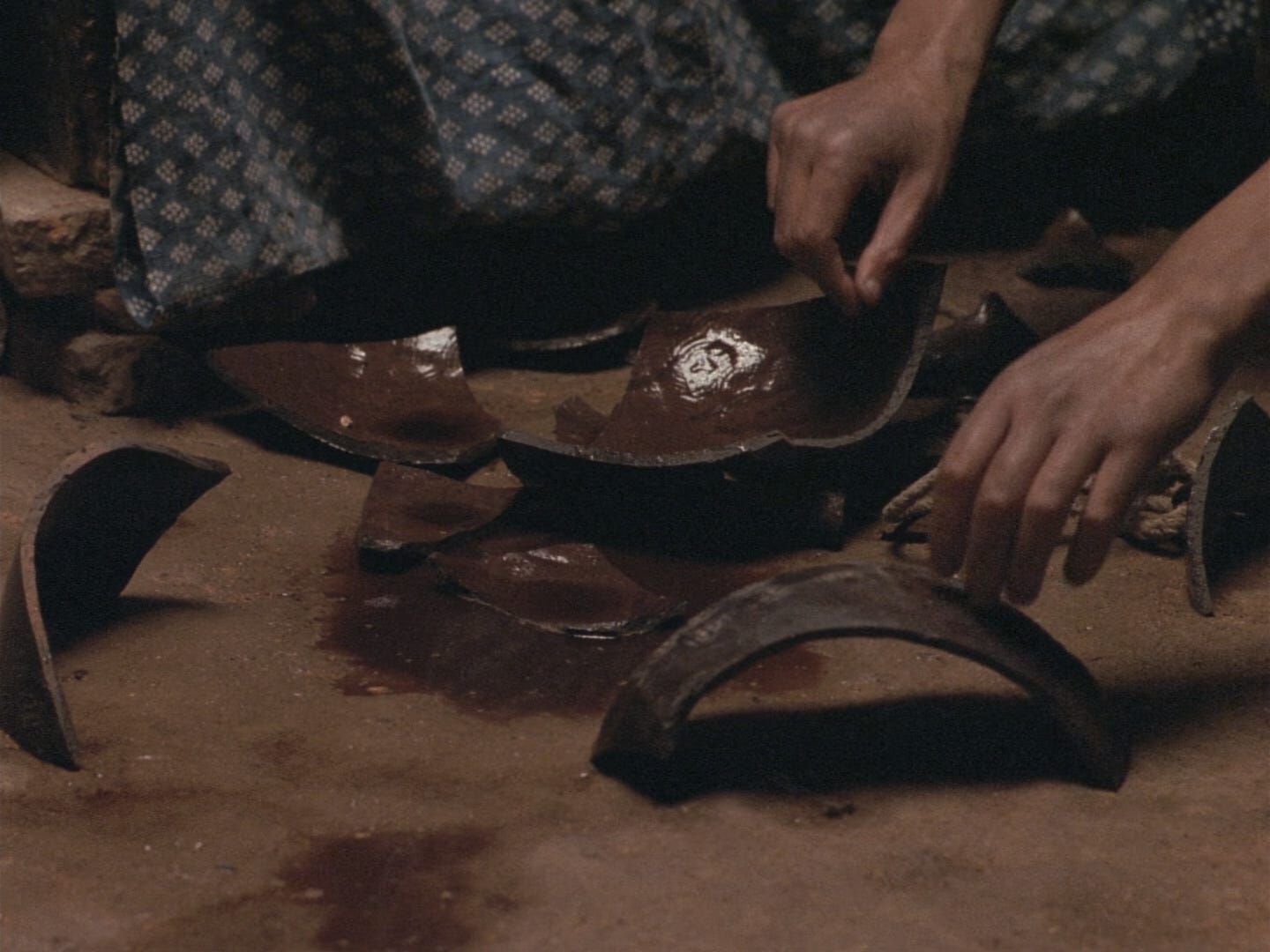Hands hover over broken brown pottery in "Ju Dou" (1990)