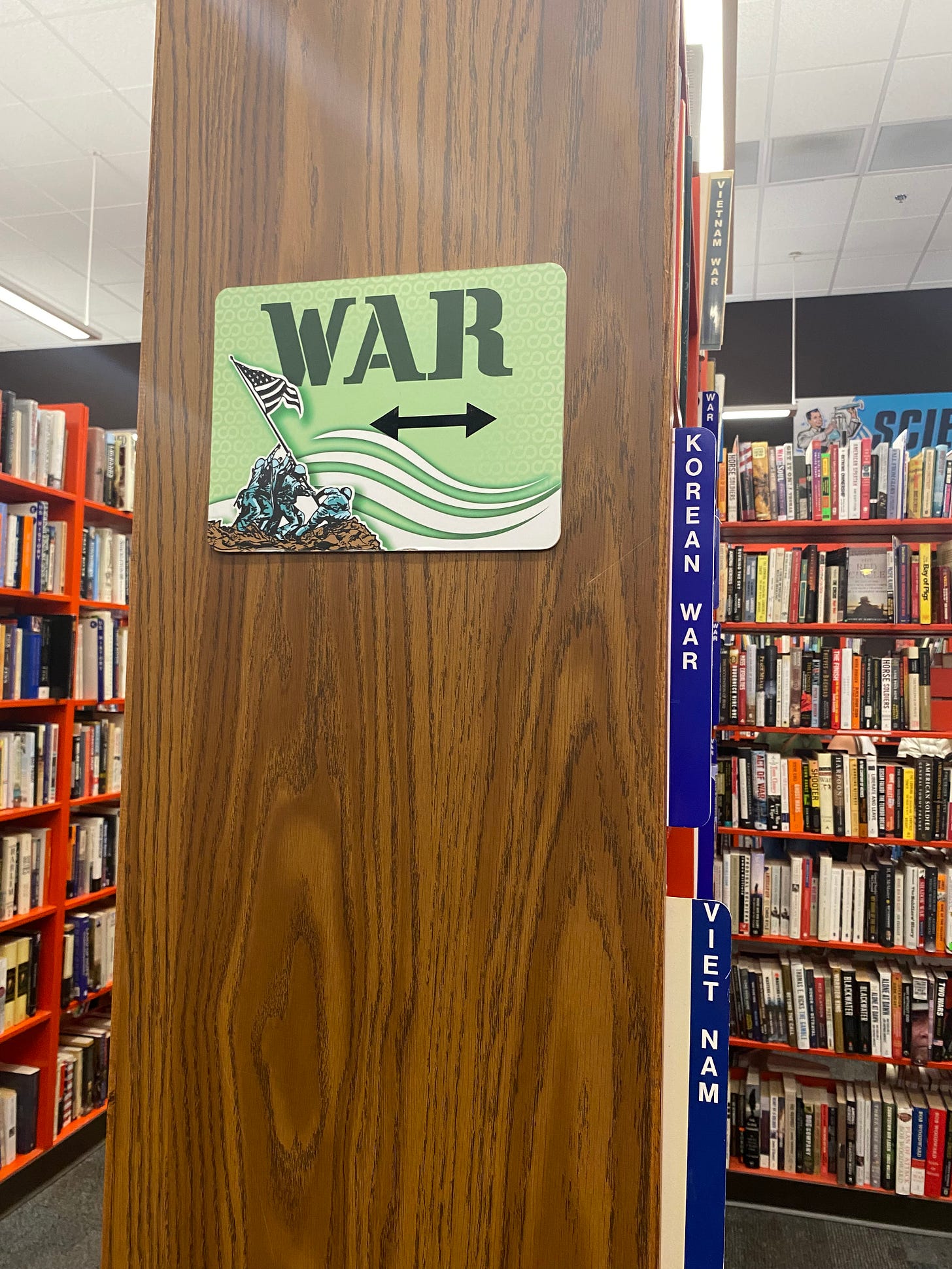 End cap of a bookcase in a bookstore. The end cap has a sign that reads, "War." Books sit on shelves on either side.