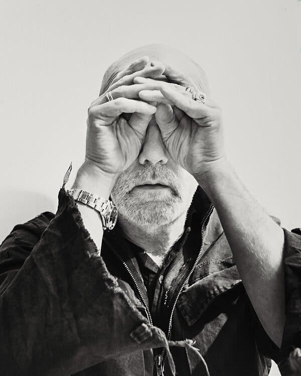 A black-and-white portrait of Stipe with his hands over his eyes.