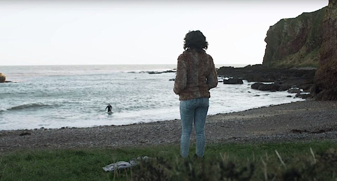 Scarlett Johansson standing with her back to the camera on a beach watching a guy wade into the water. Scarlett Johansson standing with her back to the camera on a beach watching a guy wade into the water.