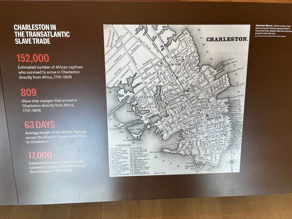 A museum display with text on the left and a map on the right.  Left: CHARLESTON IN THE TRANSATLANTIC SLAVE TRADE  152,000 Estimated number of African captives who survived to arrive in Charleston directly from Africa, 1710-1808  809 Slave ship voyages that arrived in Charleston directly from Africa, 1710-1808  63 DAYS Average length of the Middle Passage across the Atlantic Ocean from Africa to Charleston  17,000 Estimated number of captives who survived to arrive in Charleston from the Caribbean, 1670-1808  Right: There is an old, black-and-white map of Charleston, showing the Charleston Peninsula with its gridded streets. Many piers are on the east side, facing the Cooper River, and much fewer piers facing the Ashley River to the southwest, with many marshes.  caption: Charleston's Wharves Captives arrived at many wharves along the Charleston peninsula linked to international trade. Gadsden's Wharf was most active during the trade's final years. Map of Charleston, South Carolina, 1866. University of Michigan