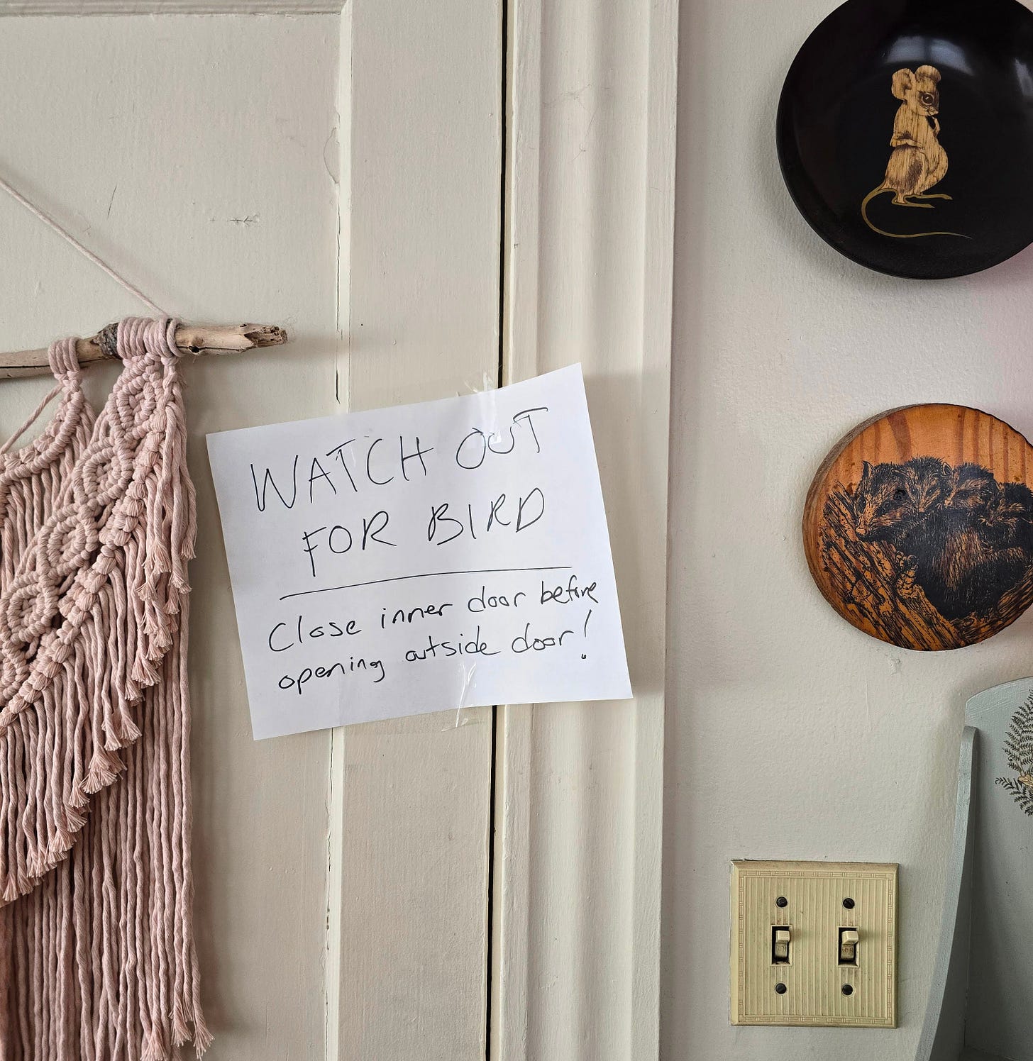 A handwritten paper sign taped to an inside door reads, "WATCH OUT FOR BIRD / Close inner door before opening outside door!"