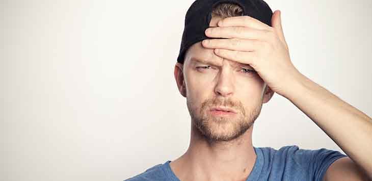 Photo of a young man holding his hand to his forehead and looking confused.