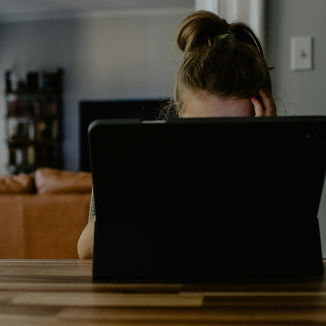 woman in white tank top sitting on chair using black laptop computer