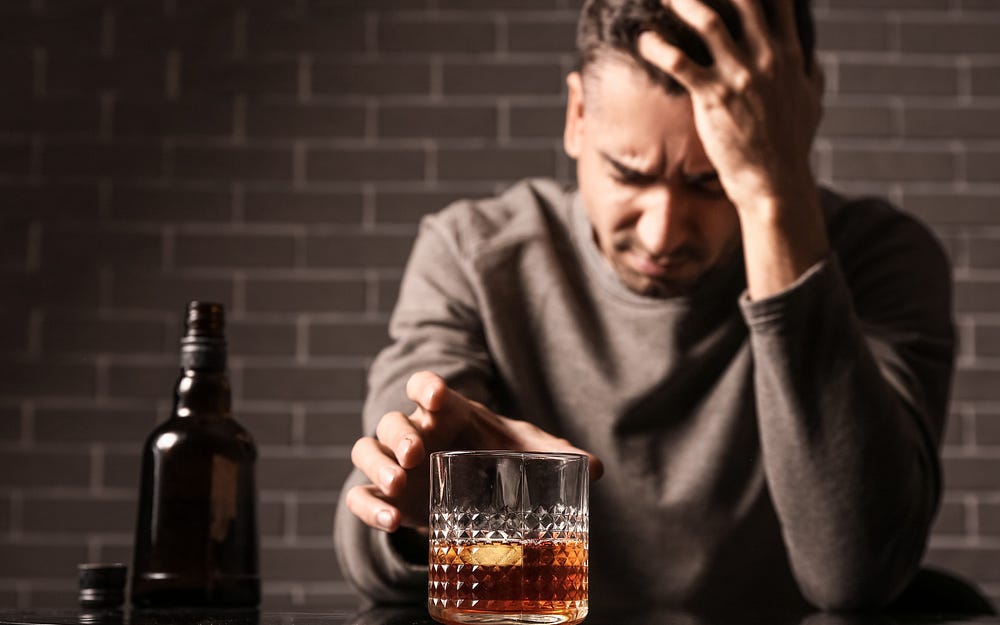 man with hand on head, reaching for a glass of booze. Greys and brown palette