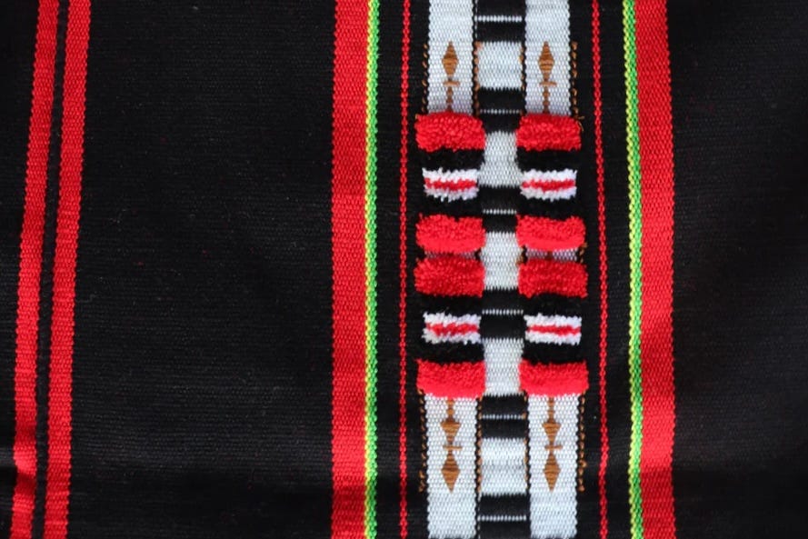 Woven shawl featuring red, black, and white geometric patterns, representing the Rira design traditionally worn by Chakhesang Naga men in Nagaland, India. A woven shawl featuring red, black, and white geometric patterns representing the Rira design of the Chakhesang Naga community in Nagaland, India. Woven shawl featuring red, black, and white geometric patterns, representing the Rira design traditionally worn by Chakhesang Naga men in Nagaland, India. A woven shawl featuring red, black, and white geometric patterns representing the Rira design of the Chakhesang Naga community in Nagaland, India.