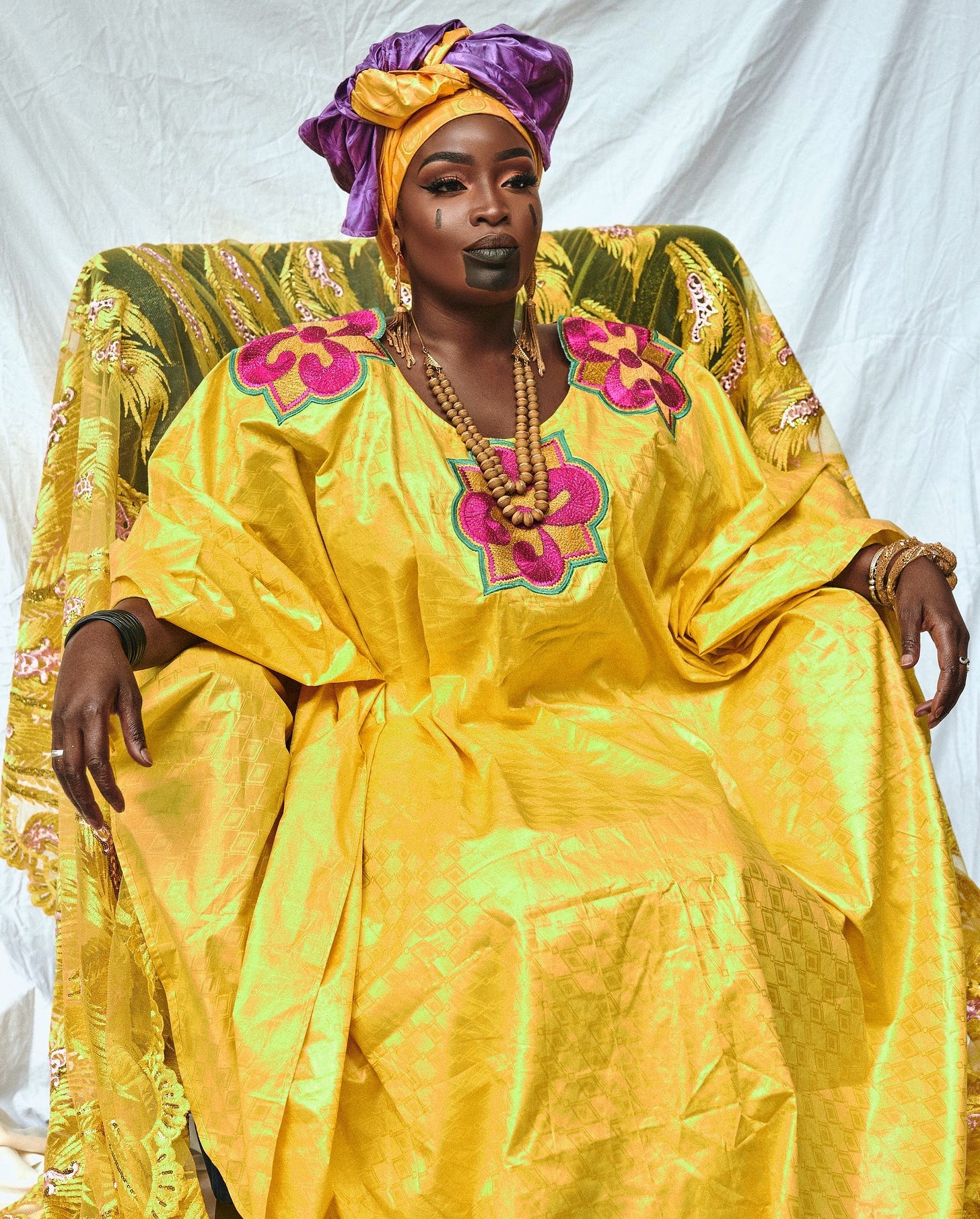 ovette Jallow in full-length Fulani ceremonial dress, seated in a position of ancestral authority. ovette Jallow in full-length Fulani ceremonial dress, seated in a position of ancestral authority.