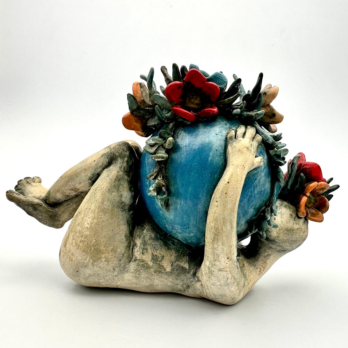 A reclining ceramic figurine holding a blue-green orb with red and orange flowers on top