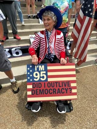 An old person in a wheelchair holding a sign

AI-generated content may be incorrect.