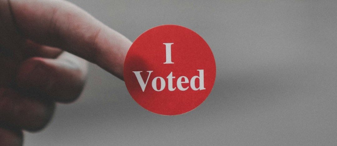 a hand holding a red button that says i vote a hand holding a red button that says i vote