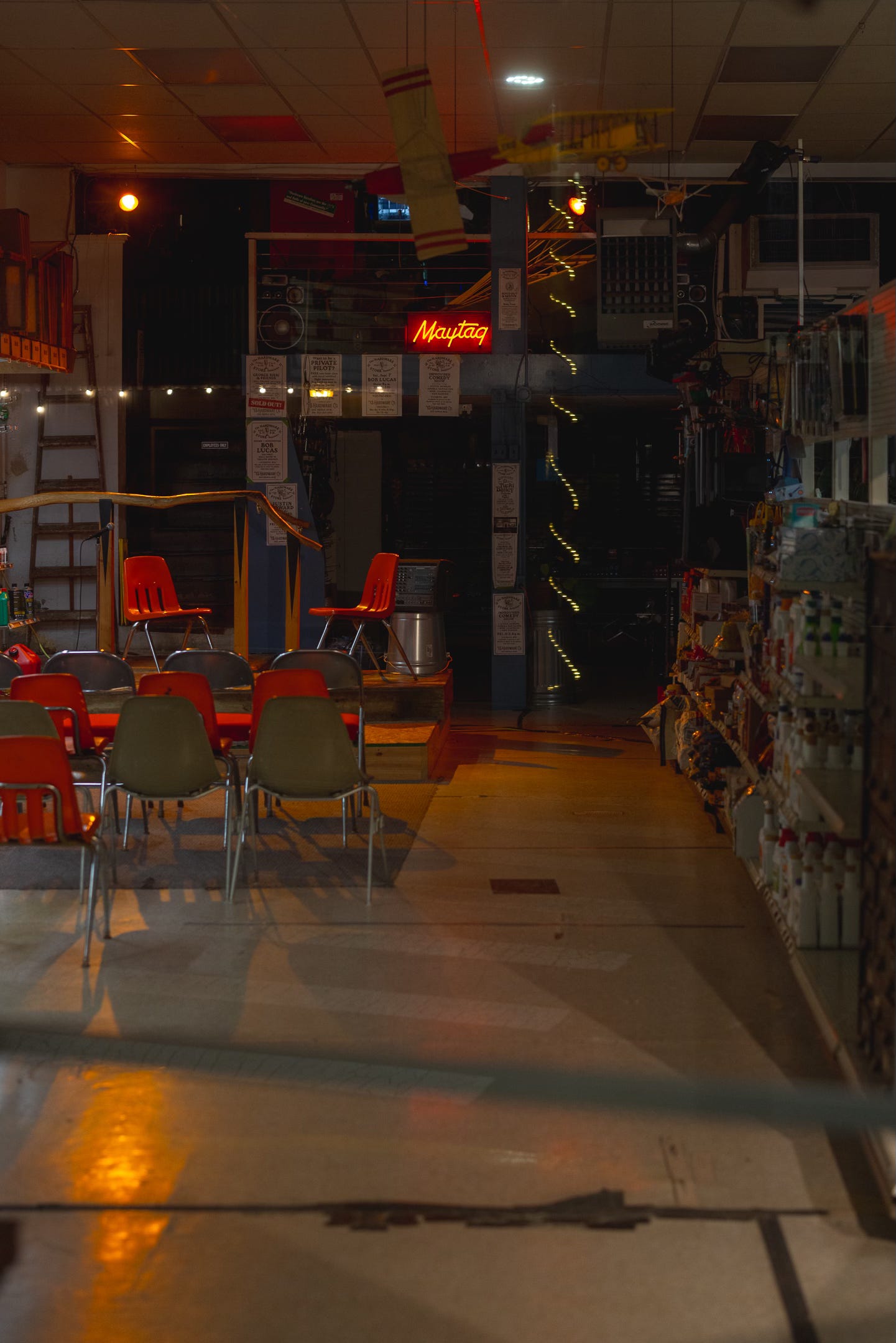 A dimly lit interior of a hardware store with empty chairs set up for an event, giving the space an abandoned yet welcoming atmosphere.