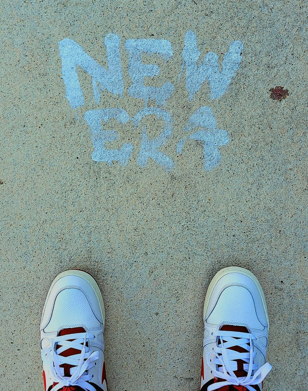 White sneakers stand before 'new era' chalked on pavement.