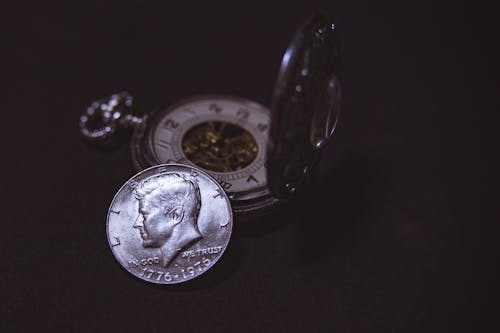 Free Close-up of a vintage silver coin with a pocket watch, symbolizing time and wealth. Stock Photo