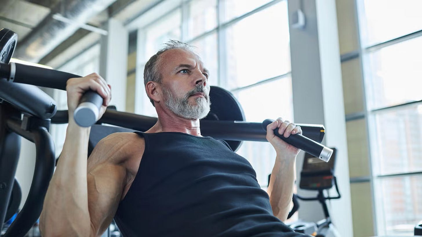 Fit older man strength training and using the machine overhead press at the gym.